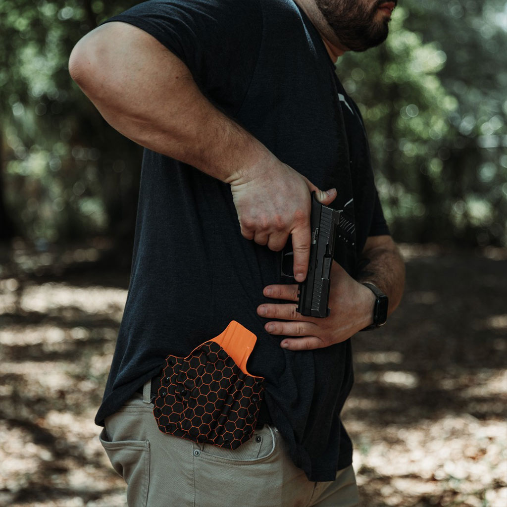A Man is drawing a firearm from his custom hexagon pattern kydex LightDraw holster attached to his belt.