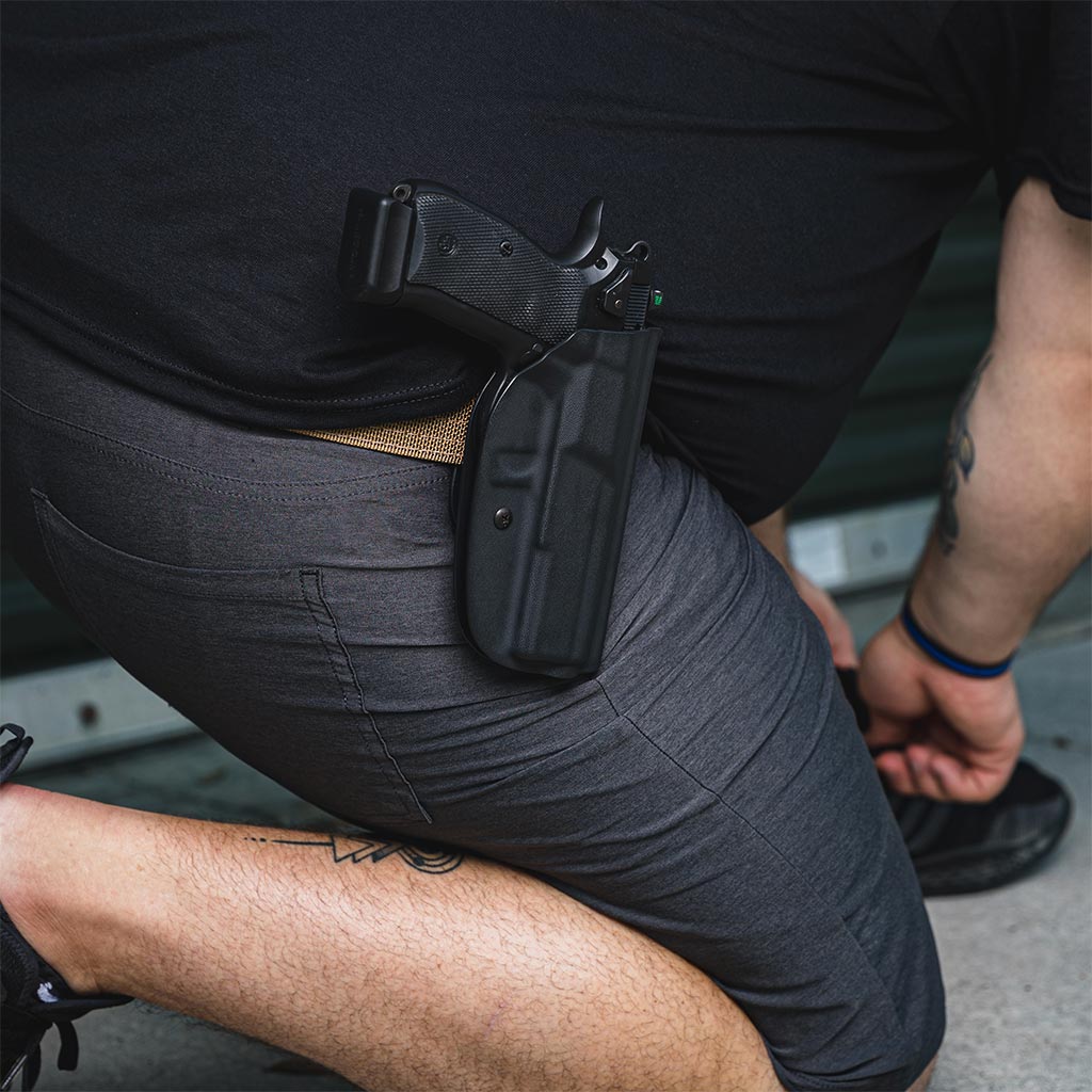 A man neals down to tie his shoe with his firearm holstered in a ProDraw holster attatched at his hip.