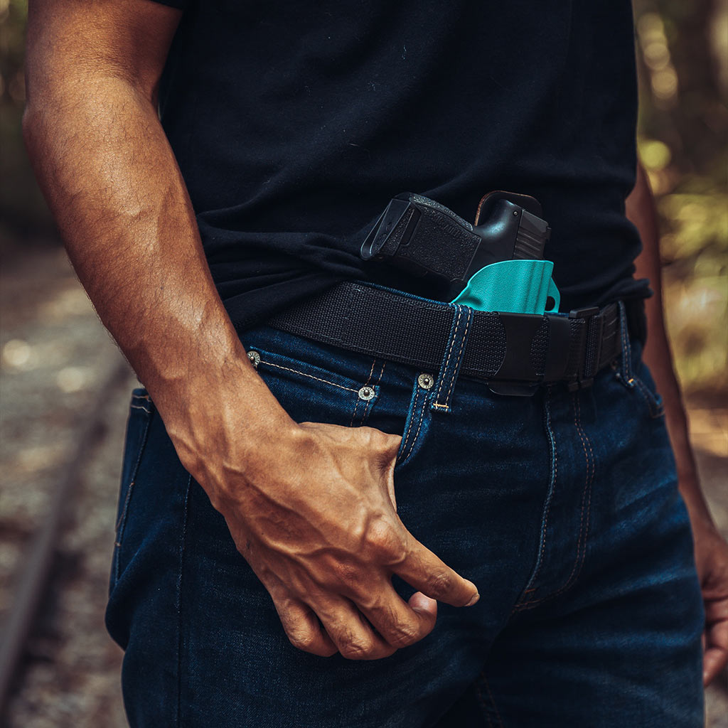 Man standing at ease with a black leather RapidTuck holster peeking from above the beltline.