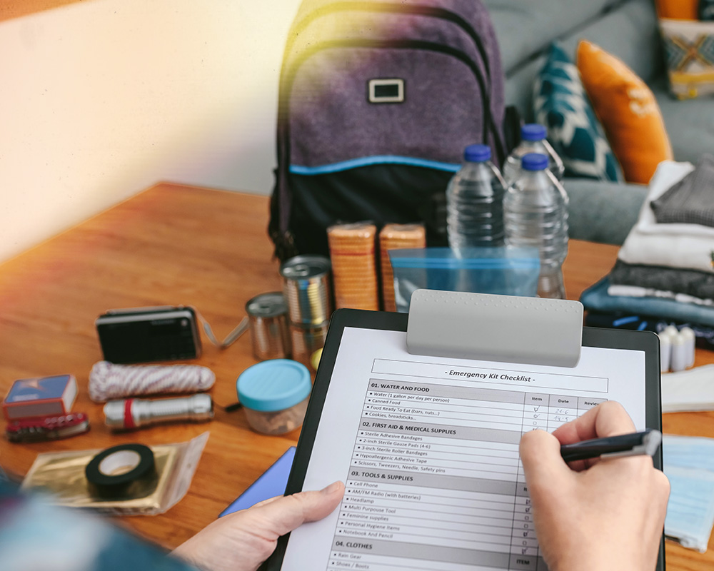 Person checking a emergency kit checklist of all the essentials they have layed on a table in front of them