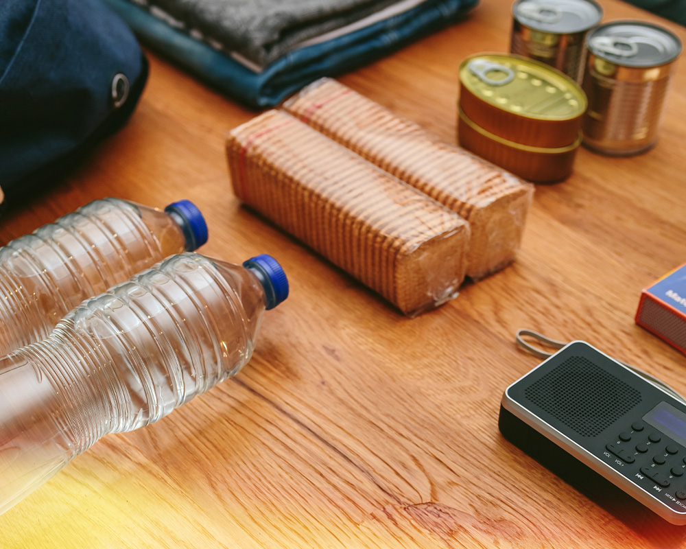 Water, cookies, canned food, a backpack and a radio layed on top of a table