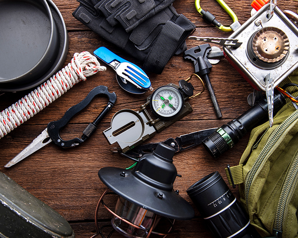 A ton of survival gear sitting on top of a table. objects as Swiss knife, rope, compass, stove, flashlight and others. 