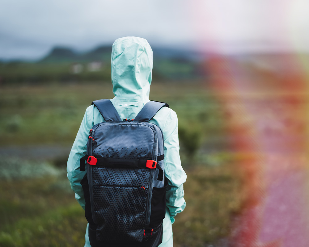 Person walking outdoors wearing a rain coat and their bag pack with mountains in the distance.