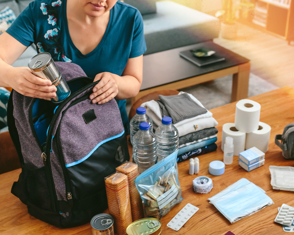 Woman packing a backpack with essentials like canned food, toilet paper, medications, etc