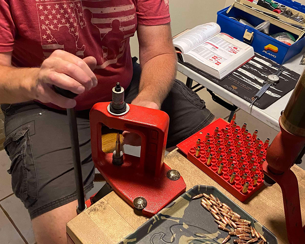 Man reloading his own ammo on a bench with a couple of tools to help the reloading process.