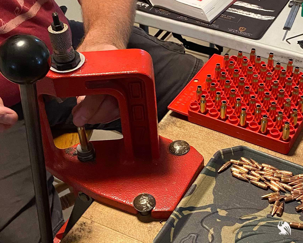 Man reloading ammo into bullet using tools to keep the bullet in place. A lot of ammo can be seen ready to be reloaded. 