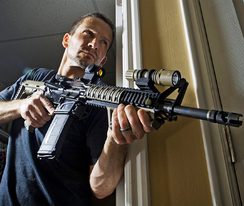 Man tactically peaking on a door frame holding his assault rifle inside his home