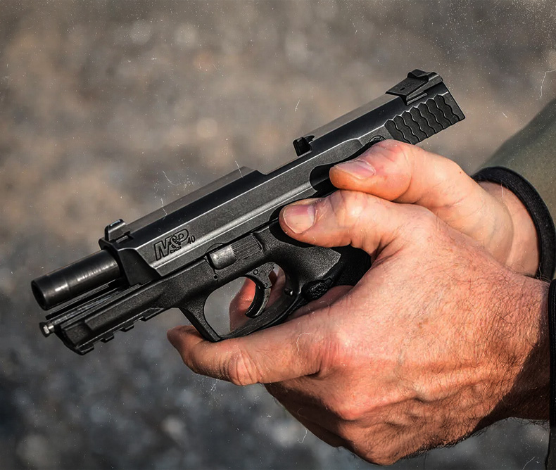 Man holding a M&P 40 using the slide lock to release the slide. 