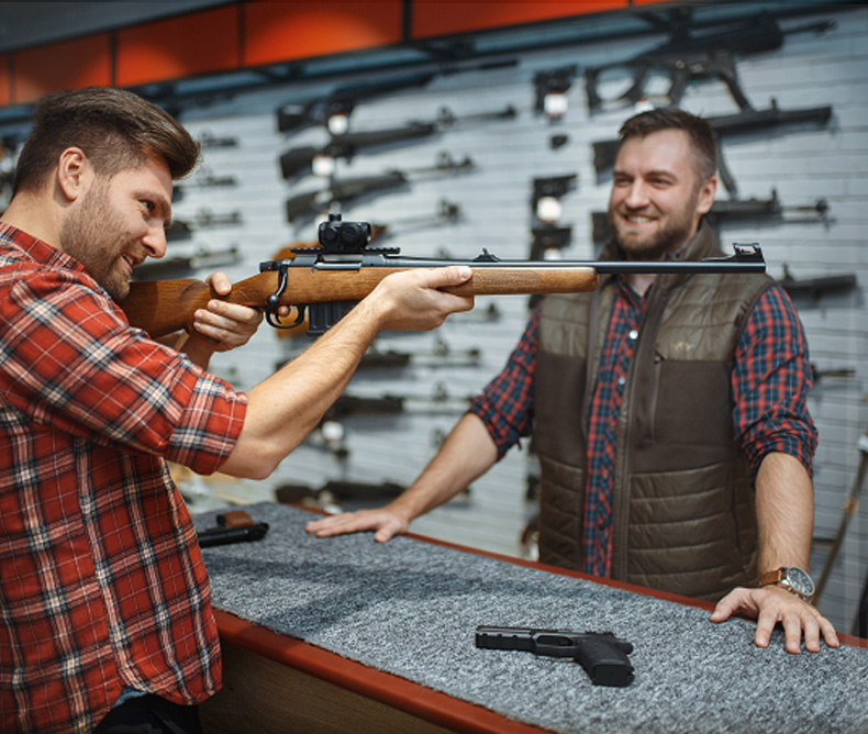 Client checking out the aim of a rifle on a gun shop with the clerk assisting him. 