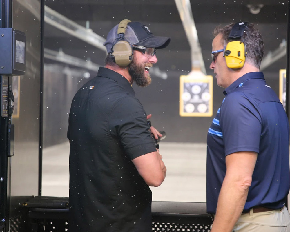 Two men chatting at a indoor shooting range.