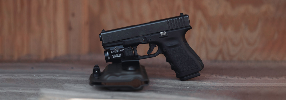 Handgun with a laser standing up and laying partially on a  gun holster from Vedder Holsters.