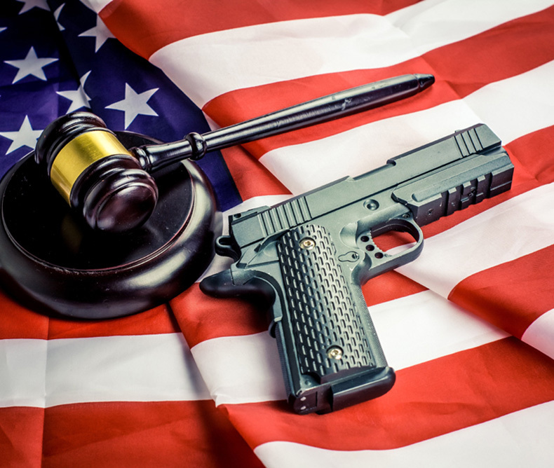 Gavel resting on top of an american flag with a handgun laying next to it on top of the flag.