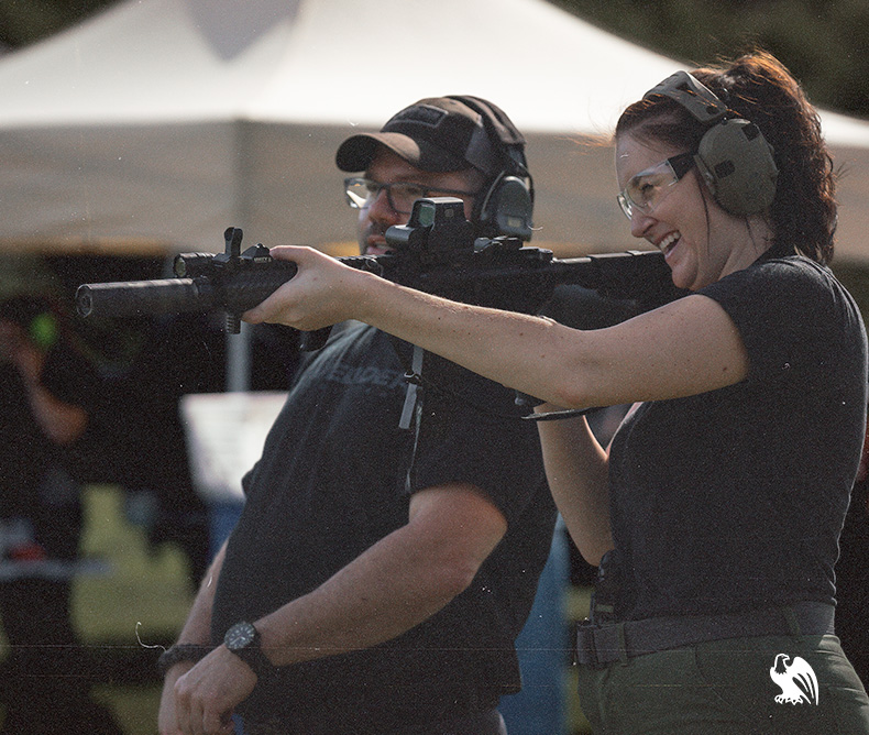 Male gun instructor and female laughing having fun at the shooting range with an assault rifle