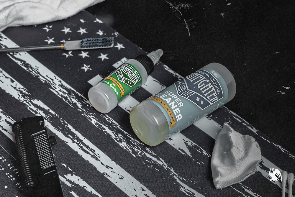 Two bottles of gun oil laying on top of a table where someone has been cleaning or greasing their handgun